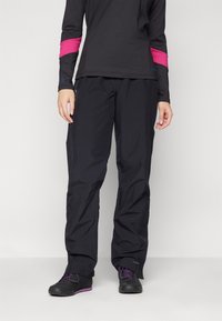 Sorte svarte vannavstøtende turbukser med rett passform og justerbar linning; kombinert med en langermet svart topp med en rosa stripe.