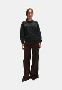 Felpa nera con scollatura tonda e polsini a costine, abbinata a pantaloni in corda marroni a gamba larga. Modello in piedi davanti a uno sfondo bianco.