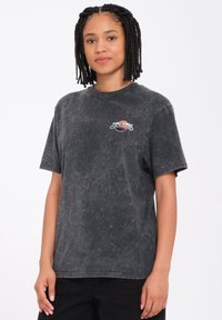 Czarny t-shirt z krótkim rękawem o subtelnej fakturze acid-wash i kolorowym graficznym logo na lewej piersi. Wykonany z bawełny.