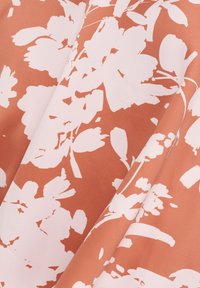 Blumenstoff mit großen weißen Blumen auf einem korallenfarbenen Hintergrund. Der Stoff wirkt glatt mit einem leichten Glanz und einer weichen Textur.