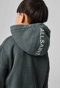 Felpa con cappuccio di colore verde scuro, caratterizzata da tessuto strutturato e un importante logo bianco sul retro del cappuccio. Design classico con vestibilità comoda.