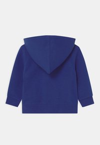 Námořnická modrá mikina s kapucí vyrobená z měkkého bavlněného materiálu, s dlouhými rukávy, přední kapsou ve stylu "klokan" a pružným lemem na rukávech a spodním okraji.