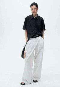 Black short-sleeve shirt, white pinstripe wide-leg pants, black belt, and black sandals. Includes a small black handbag with a strap.