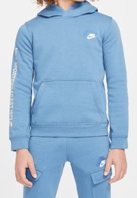 Blue cotton hoodie with a front pocket, drawstring hood, and white Nike logo on chest. Sleeve features "SPORTSWEAR EST. 1972" in gold.