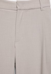 Pantalon beige clair coupe ajustée avec passants de ceinture, couture latérale et fermeture avant dissimulée, en tissu lisse.