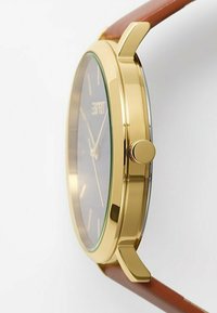 Goldfarbene Armbanduhr mit schwarzem Zifferblatt, verlängerten Indizes, einem braunen Lederarmband und einer seitlichen Krone zur Einstellung.