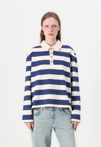 Navy and cream striped oversized long-sleeve polo with a buttoned collar and relaxed fit, featuring a straight hem and wide sleeves.