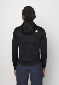 Giacca nera con cappuccio, realizzata in tessuto testurizzato, design aderente e polsini a costine. Il logo The North Face è visibile sul retro.