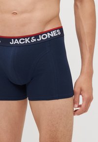 Marinblå boxershorts i mjukt tyg med en logoband i vitt med röda accenter. Inkluderar en stödjande frontficka och sömlösa ben.