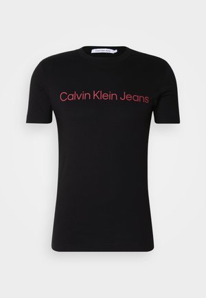 Sort kortærmet T-shirt lavet af bomuld med rund hals. Rød "Calvin Klein Jeans" logo tværs over brystet, enkelt design, ingen ekstra mønstre.