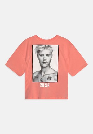 Korallrosa kortermet skjorte med et svart-hvitt portrett av en mann med tatoveringer og teksten «BIEBER» under bildet.