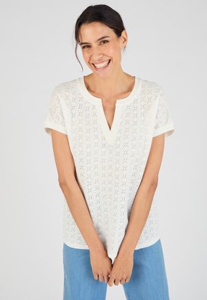 Wit kortemmers T-shirt met een V-hals, voorzien van een textuurpatroon en opgerolde mouwen. Gecombineerd met lichtblauwe jeans.