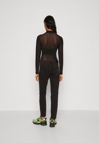 Body de malla negra de manga larga con un sutil patrón de diamantes, combinado con jeans negros ajustados y zapatillas de deporte verde brillante.