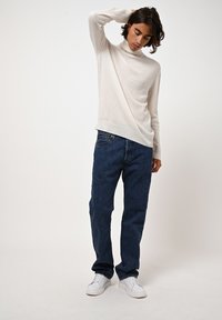 Lichtbeige coltrui van zachte stof, gecombineerd met donkerblauwe rechte denim jeans en witte sneakers. Eenvoudige en veelzijdige look.