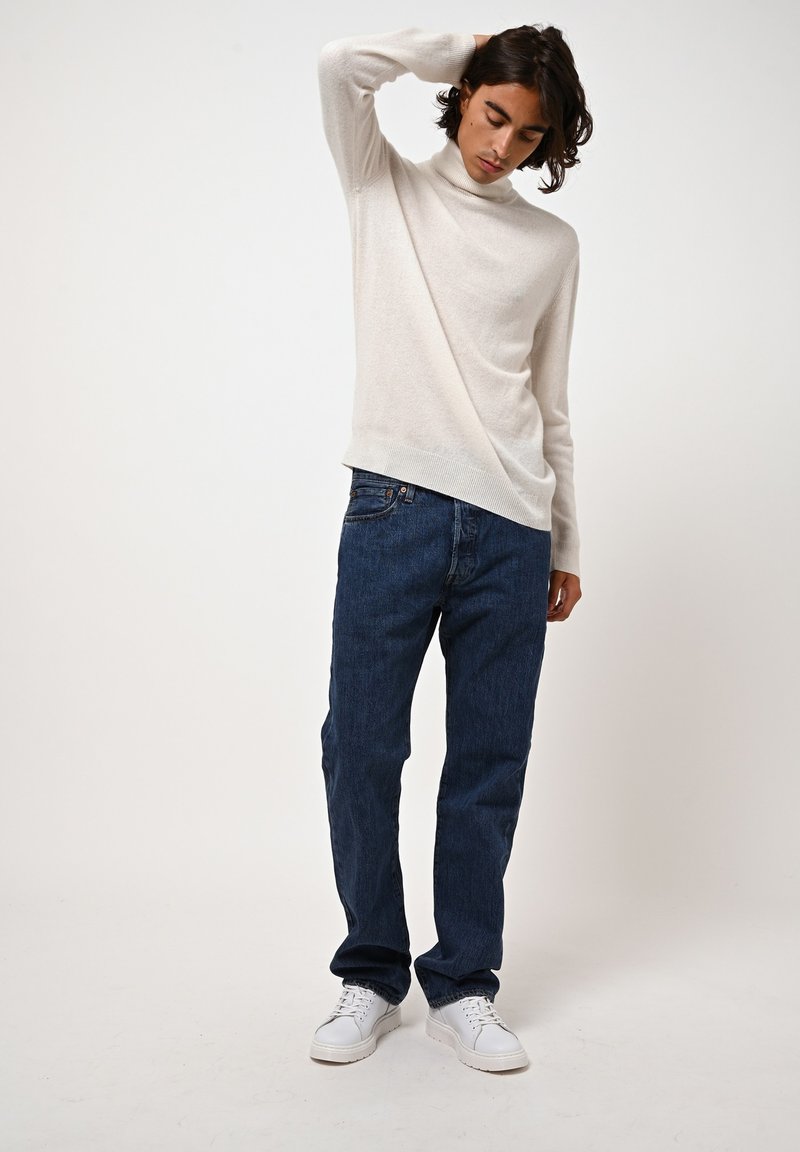 Lichtbeige coltrui van zachte stof, gecombineerd met donkerblauwe rechte denim jeans en witte sneakers. Eenvoudige en veelzijdige look.