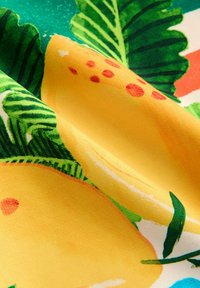 Helle Stoffe mit großen gelben Zitronen, grünen tropischen Blättern und roten Punkten in einem bunten, detailreichen Muster.