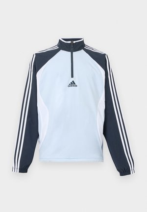 Light blue pullover jacket with a high collar, half-zip, and dark blue and white accent panels. Features three white stripes on sleeves.