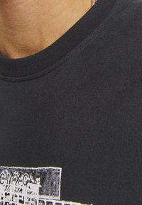 Camiseta de algodón negra con cuello redondo, que presenta un diseño gráfico impreso en blanco y acentos de colores en la parte inferior.