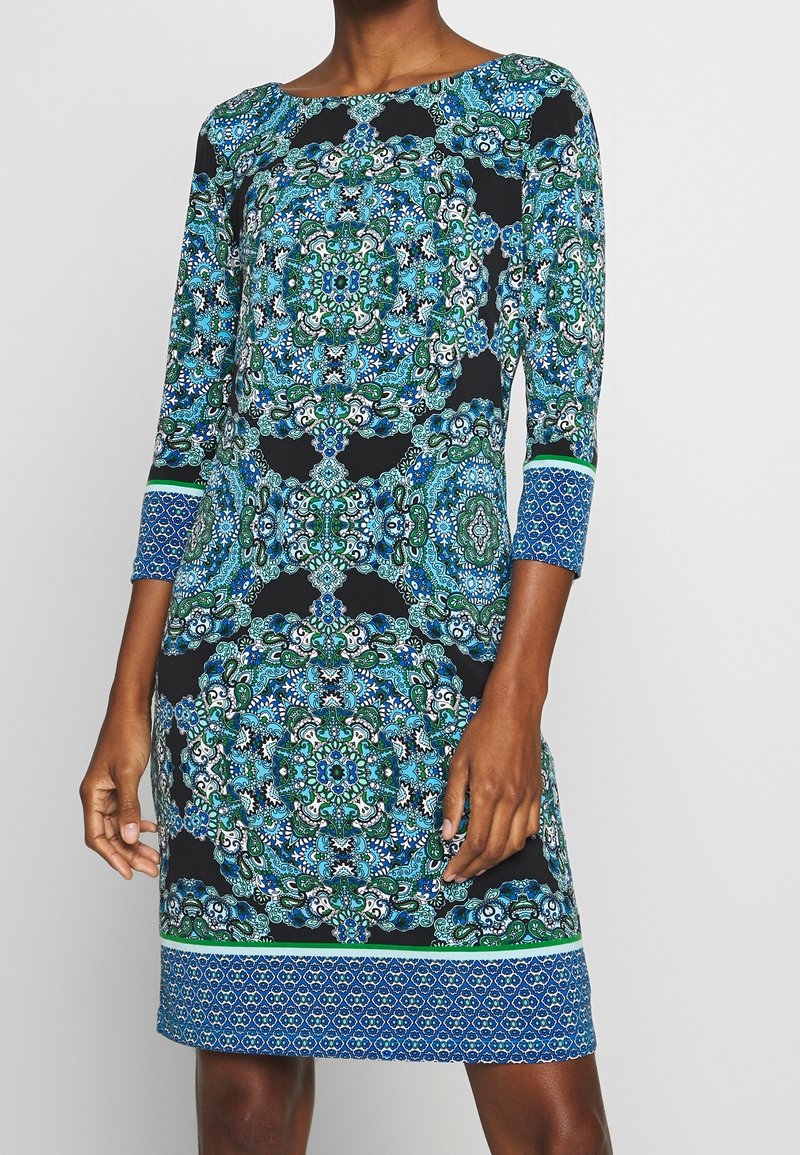 Långärmad klänning med svart bakgrund som har intrikata blå och gröna blommönster, texturerad tyg och rak passform.