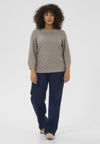 Lichtgrijze gebreide trui met een gestructureerd patroon, ronde halslijn en driekwartmouwen, gecombineerd met donkerblauwe losse jeans.