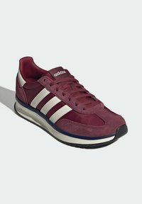 Baskets Adidas marron avec des bandes blanches, lacets à l'avant, semelle rembourrée et bout noir, présentées sur fond clair.