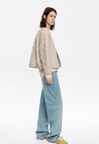 Beige quilted jacket with a loose fit, layered over a white lace top, paired with wide-leg light blue jeans and yellow footwear.