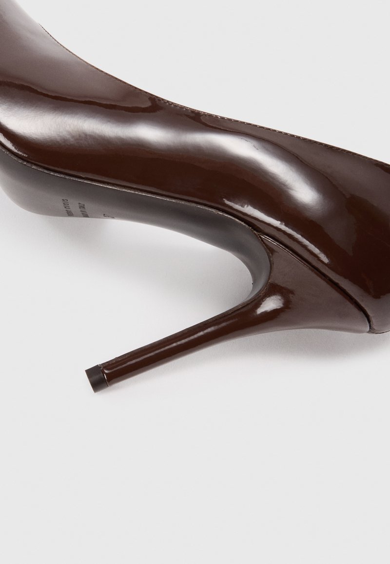 Brauner Lackleder-Pumps mit glänzender Oberfläche, spitzem Zehenbereich und schmalem Stiletto-Absatz. Glatte Textur, minimale Akzente.