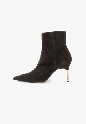 Botín de ante negro con punta afilada y cremallera en tono dorado. Cuenta con un tacón de aguja delgado con un acento texturizado dorado.