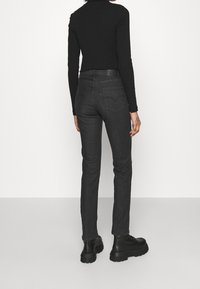 Person klädd i svart långärmad topp, mörkgrå slim-fit jeans och svarta grova snörstövlar, stående mot en enkel vit bakgrund.