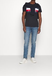 Námořnické tričko s vodorovnými červenými a bílými pruhy, spárované s světle modrými džíny a bílými teniskami. Svetr uvázaný na ramenou.