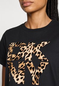 T-shirt nera con una grande grafica leopardata "DKNY". Il materiale è cotone, con un classico design a girocollo e maniche corte.