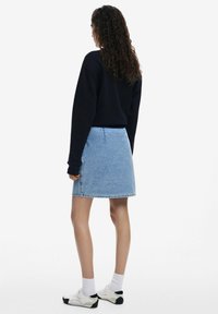 Falda de mezclilla en azul claro, de corte A con un dobladillo sin terminar, combinada con una blusa negra de manga larga y calcetines blancos con zapatos deportivos.