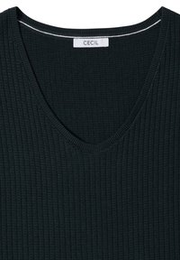 Haut tricoté noir à côtes avec col en V, étiquette blanche de la marque "CECIL" cousue à l'intérieur de l'encolure.
