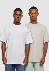 To korte ærmet t-shirts præsenteret. Den ene er hvid, den anden er lys beige, begge i en afslappet pasform. Blødt bomuldsstof, ensfarvet design.