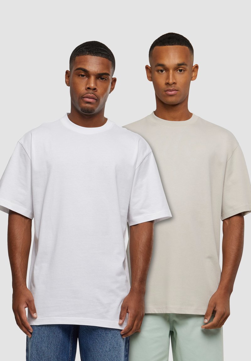 To korte ærmet t-shirts præsenteret. Den ene er hvid, den anden er lys beige, begge i en afslappet pasform. Blødt bomuldsstof, ensfarvet design.