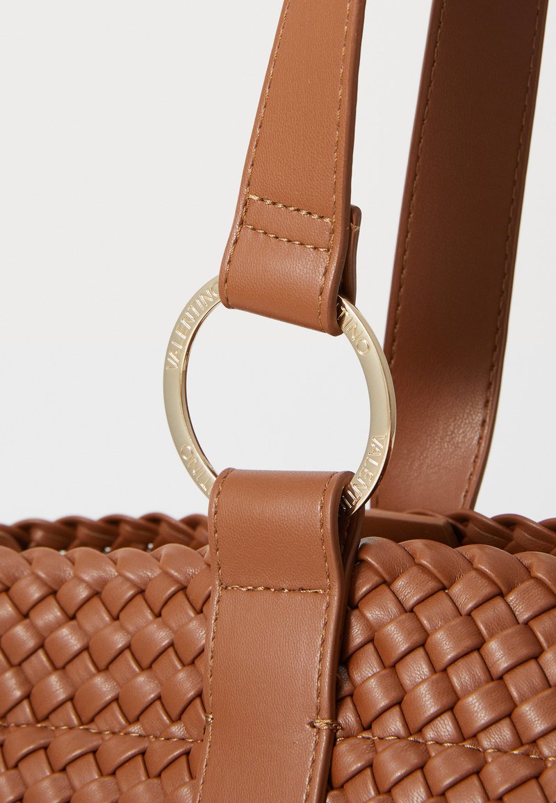Braune, geflochtene Ledertasche mit einem glatten Riemen. Sie verfügt über goldene Beschläge und einen markanten, kreisförmigen Ring mit dem eingravierten Markennamen.