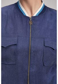  Marinblå bomberjacka med dragkedja framtill, ribbad vit och blå krage, två bröstfickor och en strukturerad tygfinish.