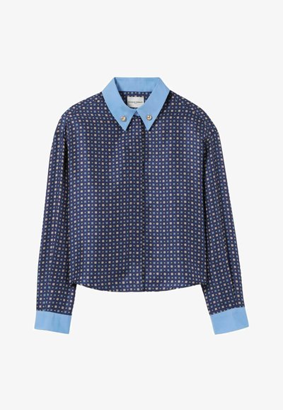 Camisa recortada en tejido azul marino con un pequeño patrón geométrico. Cuello y puños en un tono azul claro. Presenta acentos de botones brillantes en el cuello.