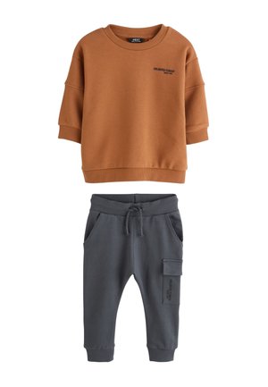 Braunes Sweatshirt mit kurzen Ärmeln und schwarzem Text, kombiniert mit dunkelgrauen Jogginghosen mit Front- und Cargotaschen.