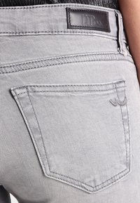 Jean en denim gris à la texture douce, avec un patch en cuir portant l'inscription "LTB" et une seule poche arrière avec des détails de couture subtils.