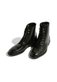 Stivaletti neri in pelle con dettagli a brogue, accenti cuciti e una finitura morbida e lucida. Presenta sei occhielli e una punta rotonda.