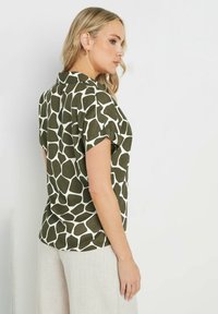 Camicetta a maniche corte di colore verde oliva con stampa di giraffe bianche. Presenta un colletto e una vestibilità rilassata, realizzata in tessuto leggero.