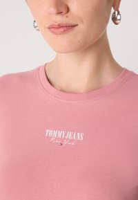 Rúžová bavlnená tričko s okrúhlym výstrihom, s bielym potlačeným logom "TOMMY JEANS New York". Hladká textúra a voľný strih.