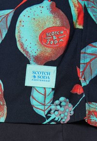 Kukkakuosinen kangas, jossa eloisa sitruuna- ja lehtikuviointi. Mukana näkyvä sininen etiketti, jossa lukee "Scotch & Soda Amsterdam".