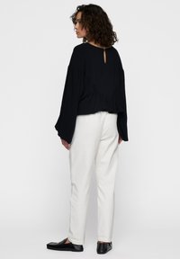 Top nero a maniche lunghe con apertura a forma di chiave sul retro, dettaglio arricciato in vita, abbinato a pantaloni bianchi e scarpe flat nere.