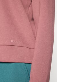 Ροζ φούτερ με απαλό ύφασμα και ριμπ μανσέτες, με στρίφωμα που έχει ραφή. Διακοσμημένο με μικρό λογότυπο "ONLY" κοντά στο κάτω μέρος.