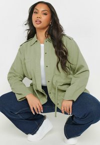 Ljus olivgrön, oversized jacka med knappframsida, bröstfickor och justerbar dragsko. Matchad med mörkblå vida jeans och vita sneakers.