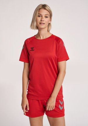 Rød sportstrøje med korte ærmer, struktureret stof og sort logo. Kombineret med røde shorts med sølvfarvede chevron-detaljer.