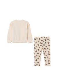 Haut crème à manches longues avec des boutons dans le dos et des détails en volants, associé à un legging crème à motif de cœurs marron.