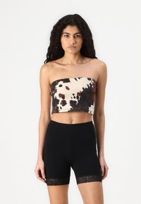 Strapless croptopp i beige med brun og svart sprutmønster, paret med svarte shorts med blondekant ved lårene.